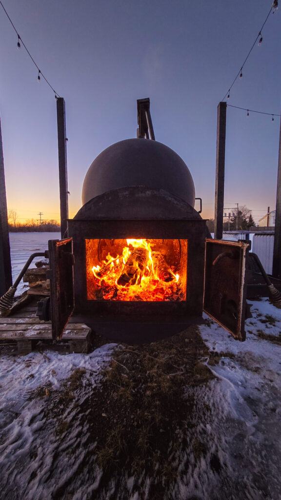 A roaring fire in the 420-gallon firebox of the thousand-gallon smoker kicks off the day's cooking process in the early morning, at the Neptune Drive-In Theatres, in Shediac, New Brunswick.