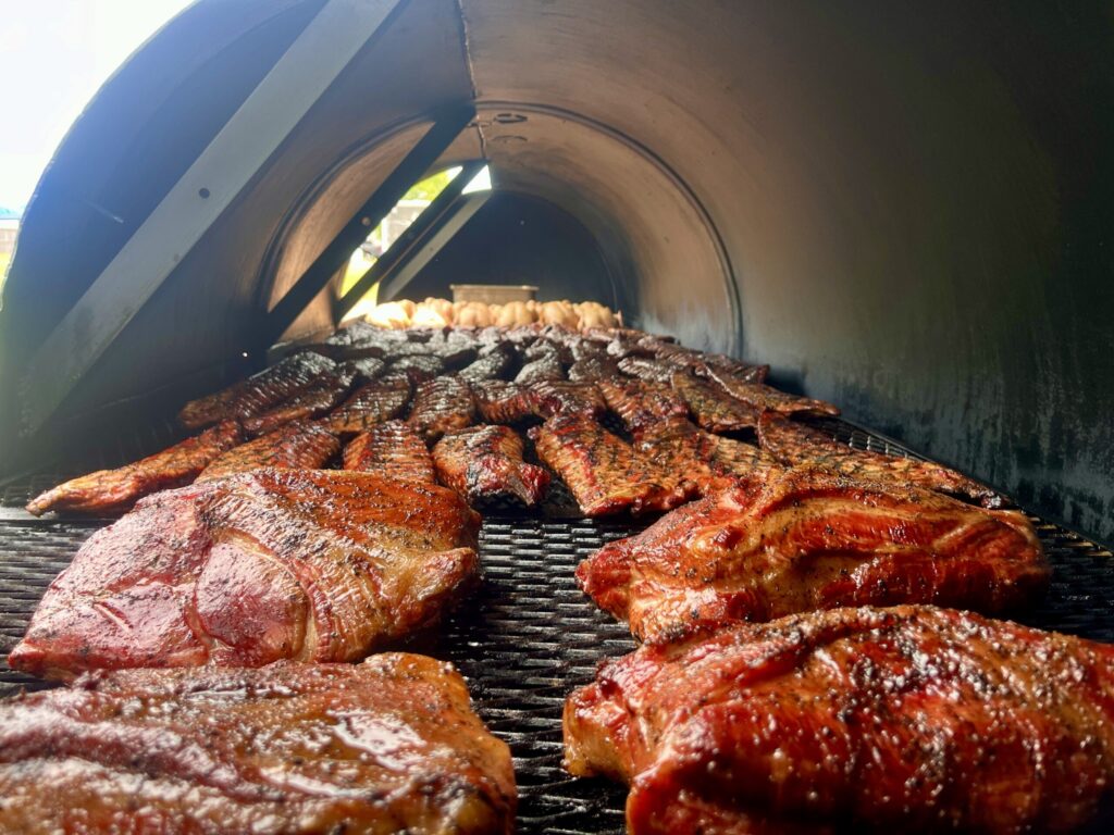 Hundreds of pounds of meat inside the thousand-gallon Morse et Marteaux BBQ smoker. In the foreground are pork shoulders, followed by dozens of racks of ribs, and many dozens of smoked chickens.