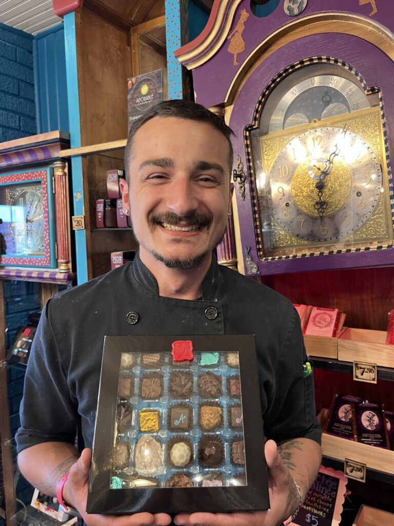 Lucas, Adorable Chocolat's Master Chocolatier, is posing with a box of chocolates in Adorable Chocolat's boutique in Shediac.