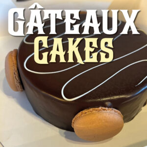 A classic Voltaire chocolate mousse cake decorated with a white icing swirl and chocolate macarons.