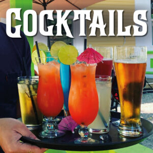 A Moque-Tortue server holding a tray of various patio-style drinks - cocktails in hurricane glasses, tall beers, lemonades, and parasols. Photograph taken on the patio of Le Moque-Tortue, in Shediac, NB