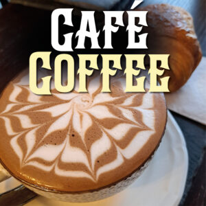 An artfully-decorated latté in a large cup served with a pain au chocolat on the side. The words "Café Coffee" are featured above.