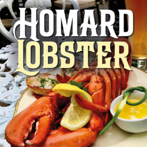 A lobster laid out upside-down on a white plate with gold trim. The lobster is served with garlic bread and a ramekin of melted garlic butter. In the background is a beer in a tall glass. The table on the patio of Le Moque-Tortue, in Shediac, NB.